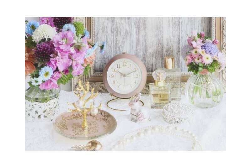机の上にキラキラ輝く小物と花と時計がある